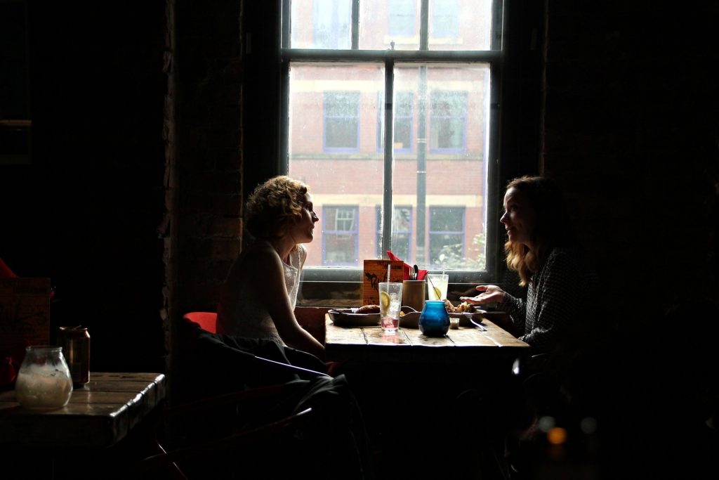 Two women sitting at a table in a dark cafe chatting and enjoying drinks.