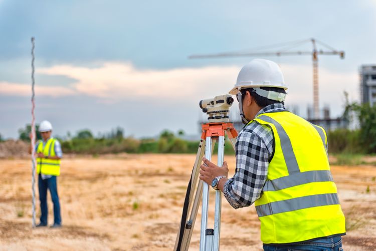 Two construction workers using a device to measure the distance between two points on a construction site.